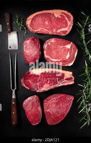 Carne, sgocchiatura piana di varie bistecche di manzo con un coltello, una forchetta, e rosmarino, su uno sfondo scuro Foto Stock