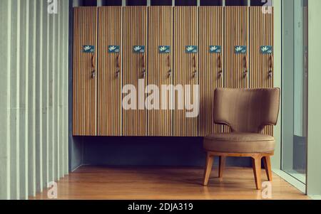 Spogliatoio con sedia marrone e armadietti in legno in palestra. Foto Stock