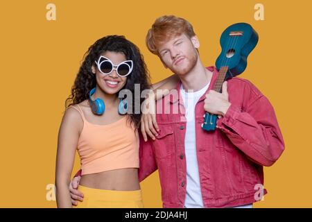 Bella giovane coppia in piedi in studio, uomo che tiene ukulele Foto Stock