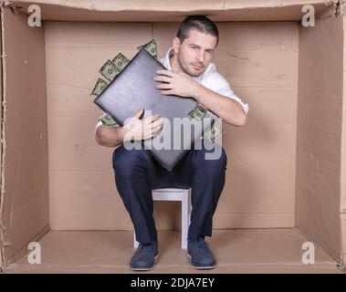 uomo d'affari con una valigetta si siede in una scatola di cartone stretta imitare un ufficio Foto Stock