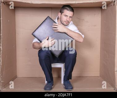 uomo d'affari con una valigetta si siede in una scatola di cartone stretta imitare un ufficio Foto Stock