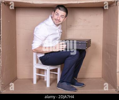 uomo d'affari con una valigetta si siede in una scatola di cartone stretta imitare un ufficio Foto Stock