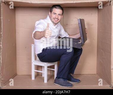 uomo d'affari con una valigetta si siede in una scatola di cartone stretta imitare un ufficio Foto Stock