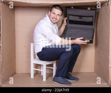 uomo d'affari con una valigetta si siede in una scatola di cartone stretta imitare un ufficio Foto Stock