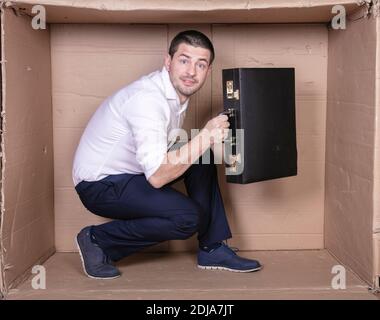 uomo d'affari con una valigetta si siede in una scatola di cartone stretta imitare un ufficio Foto Stock