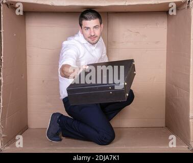 uomo d'affari con una valigetta si siede in una scatola di cartone stretta imitare un ufficio Foto Stock