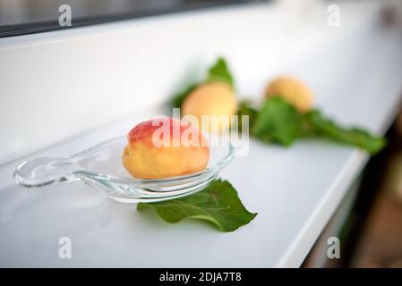 Le albicocche e le loro foglie giacciono su un davanzale bianco. Messa a fuoco selettiva Foto Stock