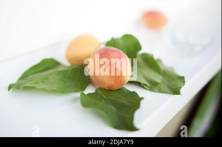 Le albicocche e le loro foglie giacciono su un davanzale bianco. Messa a fuoco selettiva Foto Stock