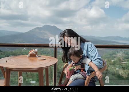 Ritratto di una madre con il suo bambino in vacanza a. un caffè che gode di succo di guava con una splendida vista Foto Stock