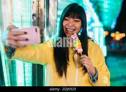 Ragazza asiatica che prende selfie con smartphone mobile nel parco divertimenti - concetto di persone e tendenze tecnologiche giovanili Foto Stock