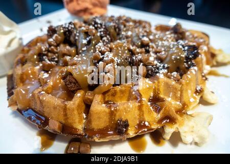 Primo piano di un dolce waffle coperto con pezzi di brownie al cioccolato e salsa di caramelle. Foto Stock