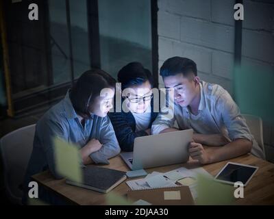 tre giovani imprenditori asiatici che lavorano tardi incontro in carica discutere aziende che utilizzano un computer portatile Foto Stock