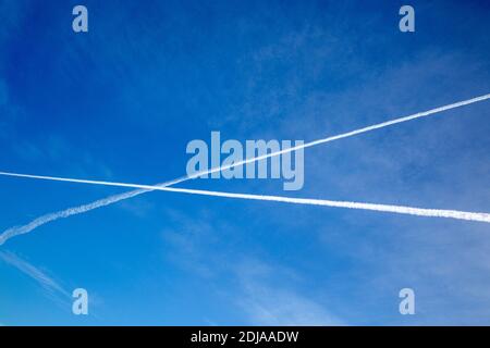 Due aerei contrails che si incrociano l'un l'altro in cielo blu profondo Foto Stock