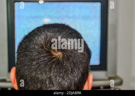 Un uomo da solo sta guardando la televisione. Foto mostra dietro l'uomo e la sua testa e anche in vecchio stile e TV a tubo c'è uno schermo sgranato. Foto Stock