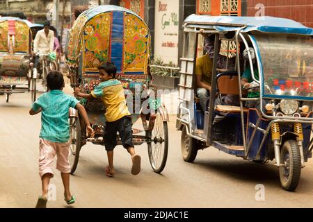 Dhaka, Bangladesh - 28 ottobre 2018: Due bambini che giocano e cercano di salire a bordo di un risciò, il mezzo di trasporto urbano più comune. Foto Stock