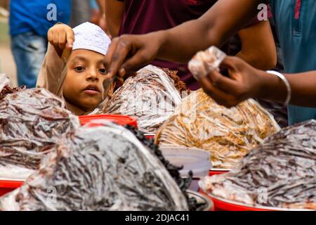 Dhaka, Bangladesh: In una bancarella di cibo di strada, un bambino indica al venditore quale pesce vuole mangiare. Il cibo di strada fa parte della cultura locale Foto Stock