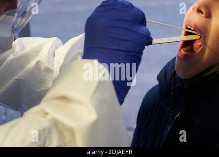 Berlino, Germania. 14 dicembre 2020. Una donna che indossa un costume, guanti e occhiali protettivi inserisce due bastoni nella gola di un bambino. Un test rapido PCR viene eseguito su un bambino di scuola a Berlino Mitte. Credit: Annette Riedl/dpa/Alamy Live News Foto Stock