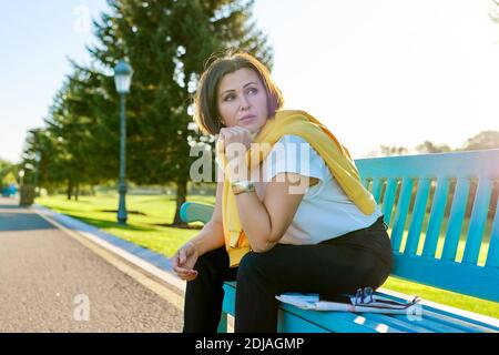 Stanca triste donna matura seduta su panchina nel parco, copia spazio Foto Stock
