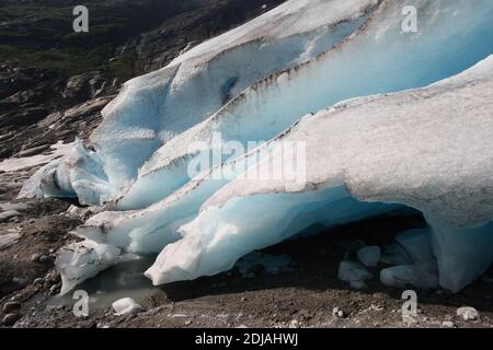 Un grande pezzo di ghiaccio proveniente da un ghiacciaio che si fonde nella montagna norvegese durante una soleggiata giornata estiva. Foto Stock