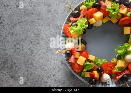 Corona natalizia di spuntini, canapes, pomodori, verdure, mozzarella per feste natalizie su sfondo grigio. Spazio di copia. Vista dall'alto. Foto Stock