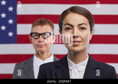 Primo piano ritratto di giovane donna politico guardando la macchina fotografica e sorridendo mentre si sta in piedi contro lo sfondo della bandiera degli Stati Uniti, copia spazio Foto Stock