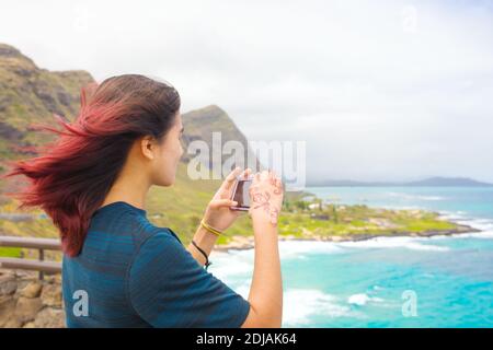 Biracial Asian Caucasian teen girl in piedi alto sopra tropicale hawaiian vista panoramica dell'oceano blu e delle montagne verdi su Oahu, Hawaii con Makapu'u B Foto Stock