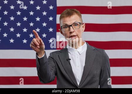 Vista frontale ritratto di donna matura politico dando voce e gesturing mentre si sta in piedi contro USA bandiera sfondo, copia spazio Foto Stock