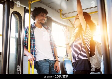 Giovane bella coppia affascinante e gioiosa è in piedi in un autobus vicino alle porte che parlano e che hanno una risata mentre viaggiano. Foto Stock