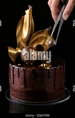 Torta al cioccolato di fantasia, isolato, sfondo nero, studio. La mano del pasticciere è presente nella cornice Foto Stock
