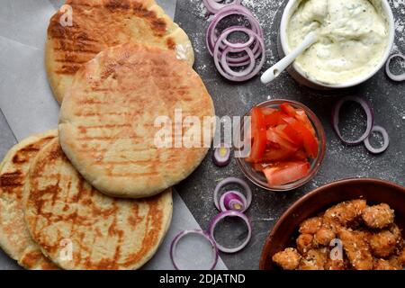 Ingredienti per preparare la pita con il pollo. Fast food sano. Vista dall'alto. Sfondo scuro. Pomodori, cipolla rossa, nocciole di pollo. Foto Stock