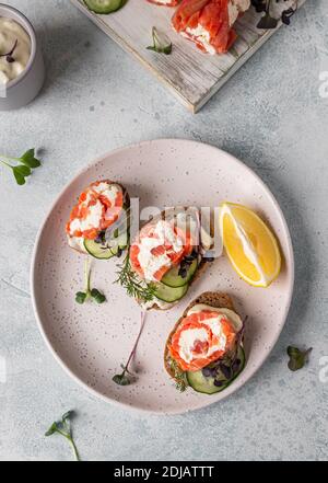 Mini panini aperti con salmone affumicato, formaggio cremoso, cetriolo e microsverde sul pane di segale, fondo di pietra grigia. Antipasto con salmone e formaggio c Foto Stock