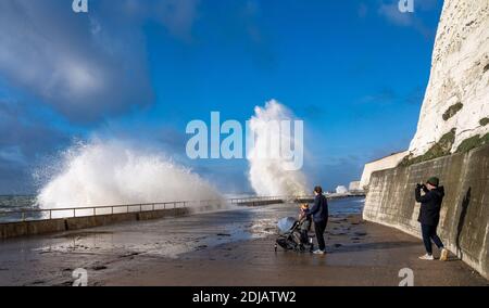Brighton UK 14 dicembre 2020 - i camminatori guardano le onde che si infrangono in una giornata ventosa lungo la passeggiata sotto la scogliera di Saltdean sul lungomare vicino a Brighton ad alta marea . Le previsioni del tempo sono per i venti e le docce più forti da spargere attraverso le parti della Gran Bretagna ma con le temperature che sono più calde che nei giorni recenti: Credit Simon Dack / Alamy Live News Foto Stock