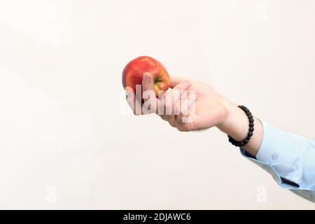 l'uomo tiene fuori la mela rossa nella sua vista laterale della mano su sfondo chiaro Foto Stock