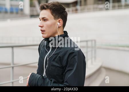 Giovane e sicuro uomo sportivo che corre allo stadio, ascoltando musica con gli auricolari, primo piano Foto Stock