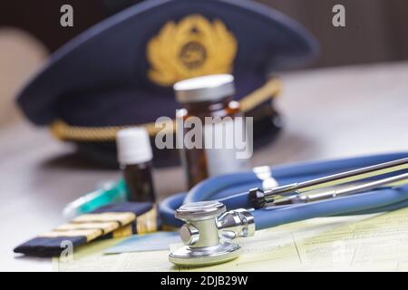 Primo piano di un aereo pilota attrezzatura cappello ed epaluete con stetoscopio del medico, forme, certificato medico e pilota e farmaci. Immagine concettuale Foto Stock