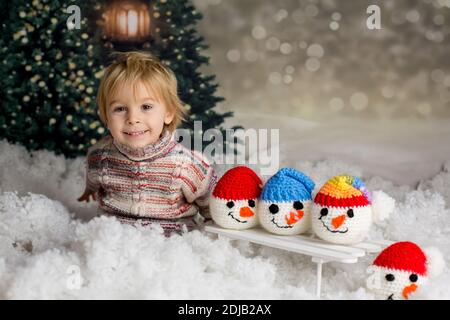 Carino bambino, con il giocattolo lavorato a maglia, giocando nella neve con colorati pupazzi di neve, sorridendo felicemente Foto Stock