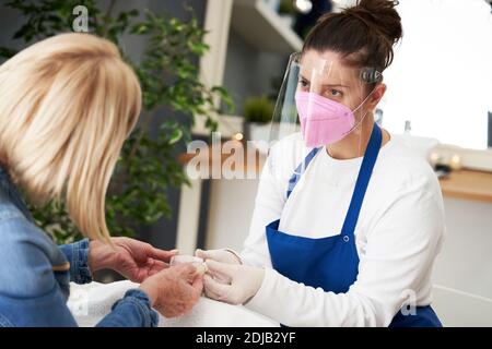 Donna anziana che indossa una maschera in manicure salone Foto Stock