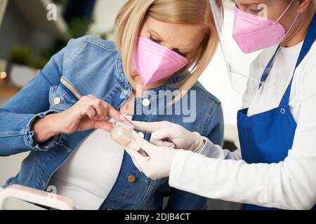 Donna anziana che indossa una maschera in manicure salone Foto Stock