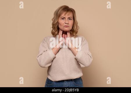 Donna caucasica matura con mal di gola che fa palpazione. Scatto in studio. Foto Stock