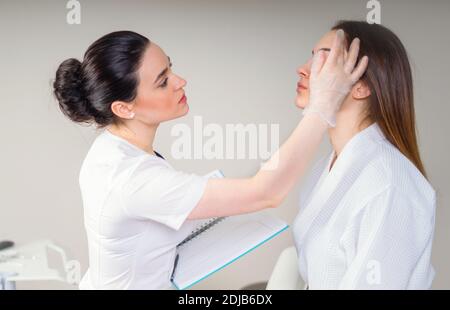 Professional cosmetico esaminando la pelle del viso della ragazza in clinica di Cosmetologia estetica Foto Stock