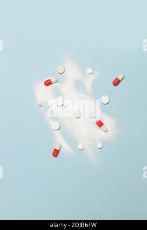 Farmaci sotto forma di polvere o capsule di diversi colori su sfondo blu. Posiziona per il testo. Giornata internazionale contro l'abuso di droghe. Foto verticale. Concetto di stile di vita sano. Disposizione piatta minima Foto Stock