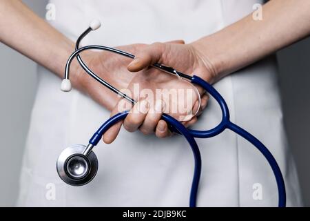 il medico femminile tiene lo stetoscopio nelle mani dietro la schiena Foto Stock