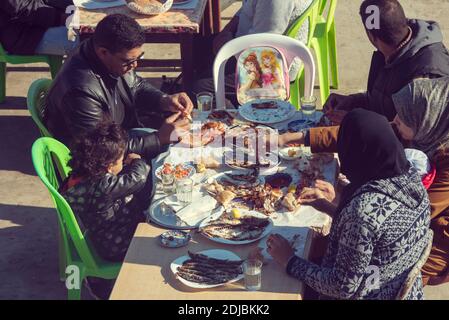 ESSAOUIRA - CIRCA GENNAIO 2018: Famiglia marocchina mangiare tradizionale pesce alla griglia sardine in un caffè di strada a Essaouira, gennaio 2018 in Marocco Foto Stock