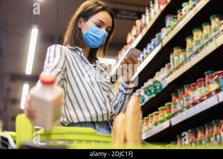 Donna in maschera con smartphone in piedi in negozio Foto Stock