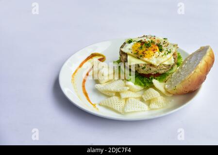 burger su un piatto con patatine. burger con polpettine e verdure come cetriolo, pomodori, lattuga e uovo semilessato e patatine fritte. Foto Stock