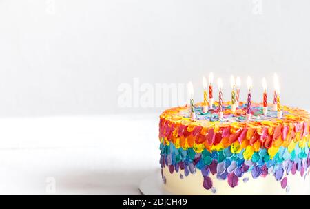 Una torta di compleanno multicolore decorata con candele brucianti. Buon compleanno saluti concetto. Foto Stock