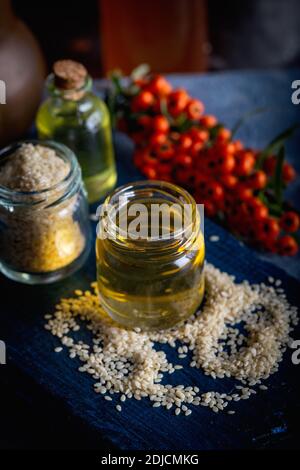 Olio di sesamo in vetro e semi. Olio di sesamo fresco in una bottiglia di vetro e semi su sfondo blu. Foto Stock