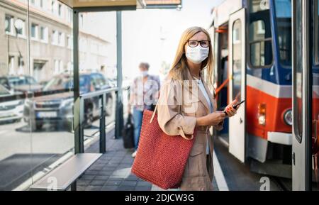 Donna anziana con smartphone sulla fermata dell'autobus all'aperto in città o in città, concetto di coronavirus. Foto Stock