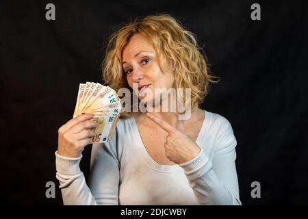 La donna bionda di mezza età punta a un fan della mano dell'euro banconote che lei tiene in mano con un puzzetto espressione Foto Stock