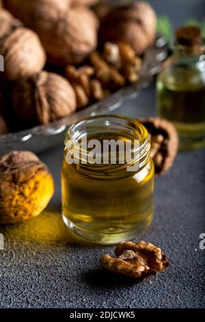 Olio di noce cosmetico e terapeutico su fondo di legno. Olio di noce in bottiglia e noci su fondo scuro. Foto Stock